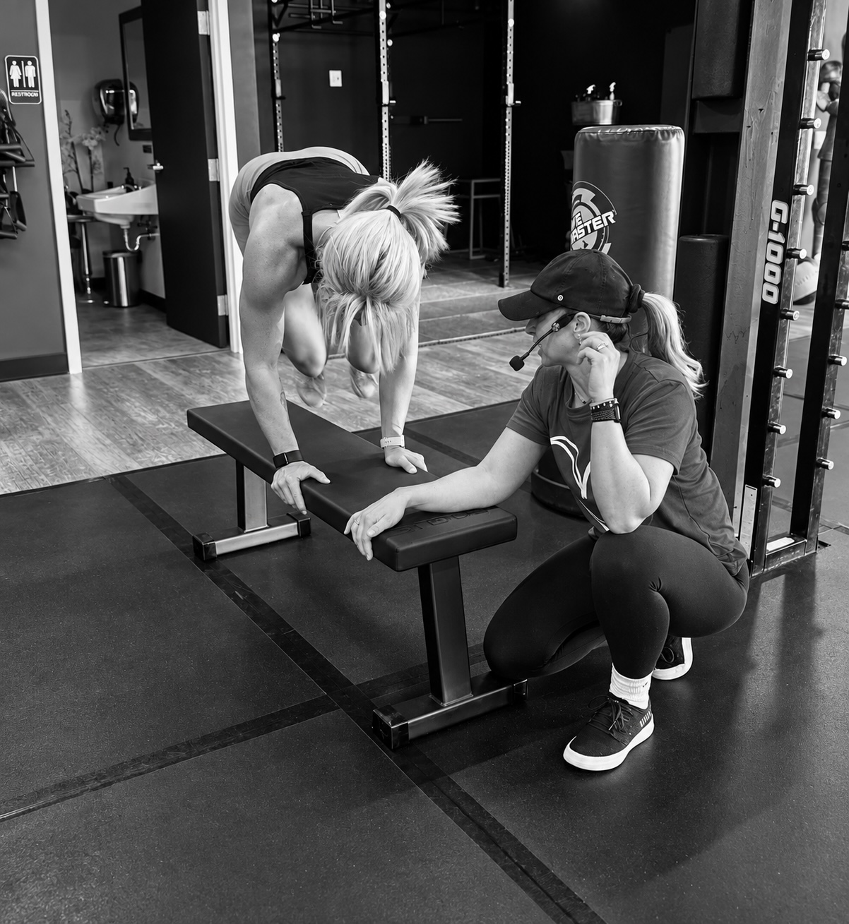 A Fitness Artist coach crouched beside a member, coaching her through a movement